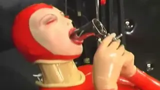 Sexy Girl Encased in Red Rubber Catsuit Loves Medical Games with Mouth Spreader and Nipple Clamps